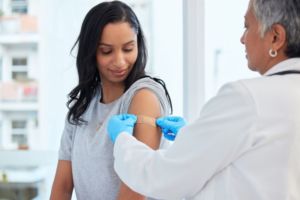 A DOCTOR PLACES A BAND AID ON THE SHOULDER OF A PATIENT.