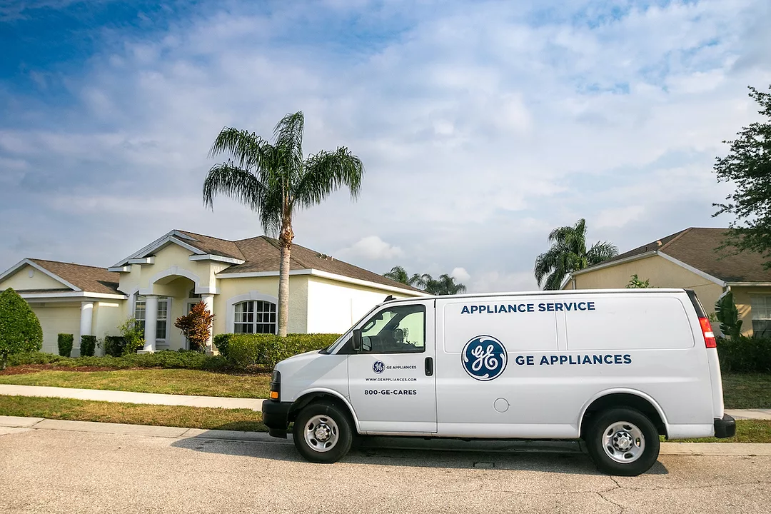 A GE APPLIANCES LABELED VAN SITS PARKED OUTSIDE OF A HOUSE. THE HOUSE HAS PALM TREE IN FRONT OF IT.