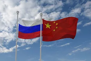 A RUSSIAN AND CHINESE FLAG WAVE NEXT TO EACH OTHER ON FLAG POLES IN FRONT OF A BLUE, CLOUDY SKY.