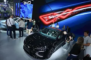 MULTIPLE PEOPLE ARE INSPECTING AN ELECTRIC VEHICLE AT A SHOW.