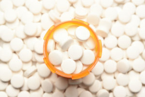 AN AERIAL VIEW OF A FULL PILL BOTTLE THAT SIST ON TOP OF A PILE OF PILLS.