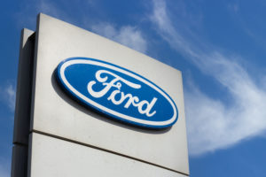 CLOSE-UP OF A FORD LOGO AGAINST A BLUE SKY.