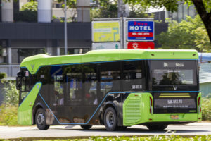 A GREEN AND BLACK ELECTRIC BUS DRIVES IN FRONT OF A SIGN. THE VINFAST LOGO CAN BE SEEN ON THE BACK OF THE BUS.