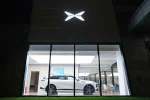 AN EXTERIOR SHOT OF AN XPENG CAR DEALERSHIP AT NIGHT. THE XPENG LOGO CAN BE SEEN ON THE OUTSIDE OF THE BUILDING. INSIDE, A WHITE XPENG CAR IS VIEWABLE THROUGH WINDOWS.