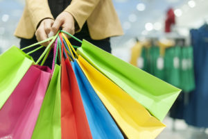 A WOMAN APPEARS TO BE HOLDING SEVERAL DIFFERENT COLORED SHOPPING BAGS.
