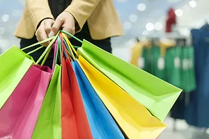 A WOMAN APPEARS TO BE HOLDING SEVERAL DIFFERENT COLORED SHOPPING BAGS.