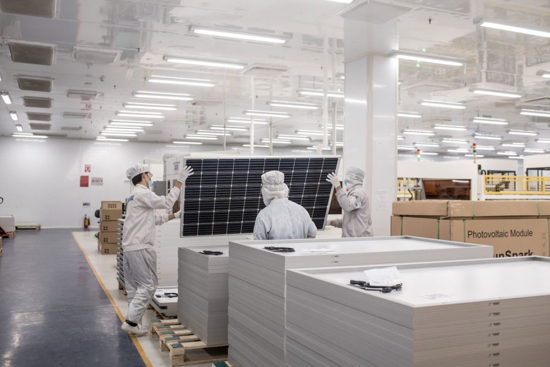 THREE PEOPLE IN HAZMAT SUITS ARE MANUFACTURING A SOLAR PANEL.