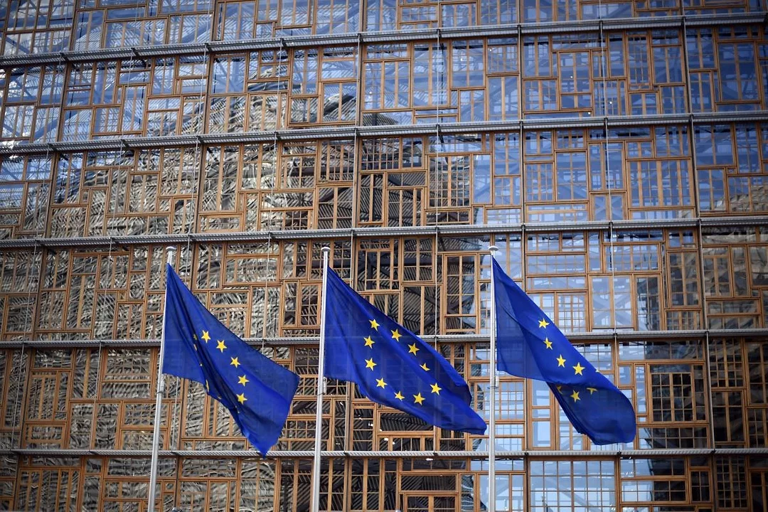 EU FLAGS ON POLES FLY OUTSIDE A GLASS-FRONTED BUILDING