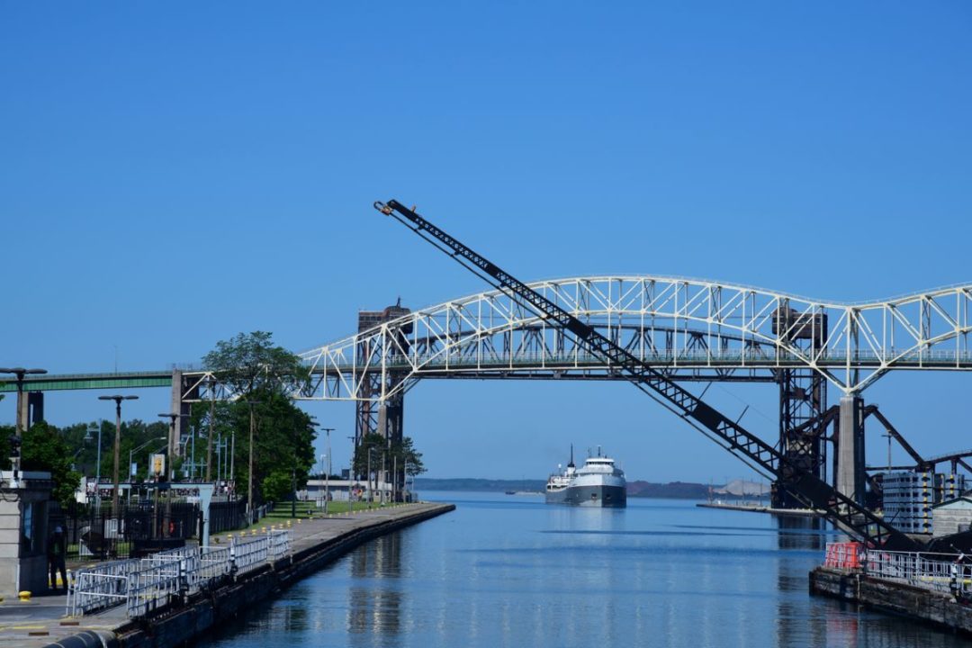 A SHIP PASSES BENEATH A BRIDGE OVER A BROAD WATERWAY