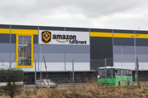 A WAREHOUSE WITH THE AMAZON FULFILLMENT LOGO ON TOP OF IT SITS UNDER A CLOUDY SKY."