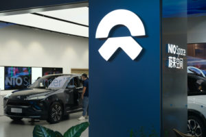 THE NIO LOGO CAN BE SEEN ON A BLUE COLUMN INSIDE OF A STORE WITH A NIO ELECTRIC VEHICLE IN THE BACKGROUND.