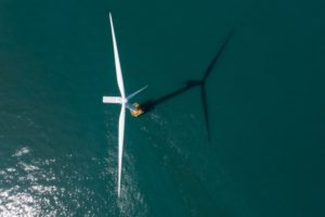 AERIAL VIEW OF A SINGLE WIND TURBINE IN A BODY OF WATER.