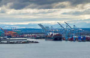 A SHIP IS DOCKED NEAR CRANES AT THE PORT OF TACOMA BELOW A CLOUDY SKY.