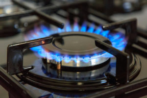 BLUE FLAMES BILLOW OUT OF THE TOP OF AN ACTIVE NATURAL GAS STOVETOP BURNER.
