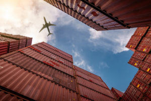 GROUND VIEW OF AN AIRPLANE FLYING OVER SEVERAL RED SHIPPING CONTAINERS.