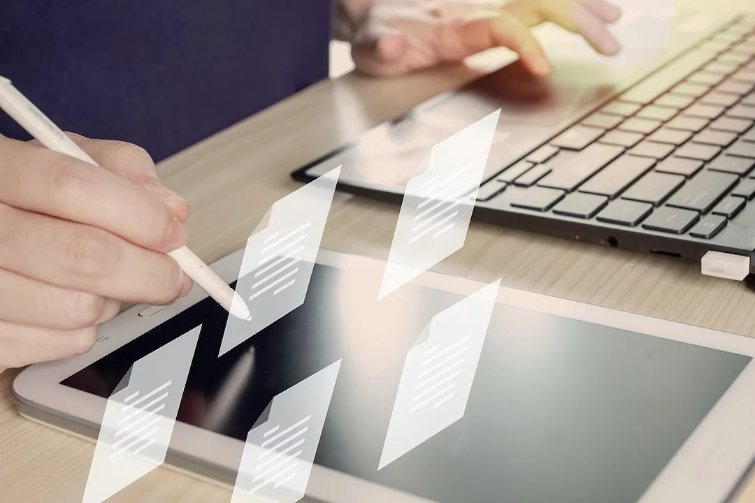 A PERSON HOLDING A PEN USES IT TO SEND AN ELECTRONIC DOCUMENT ON A TABLET. FIVE PAPER ICONS FLOAT ABOVE THE TABLET.