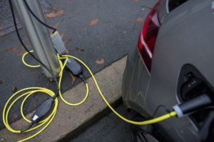 A YELLOW ELECTRICAL CAR CHARGER IS PLUGGED IN TO AN ELECTRIC VEHICLE.