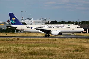 A SAUDIA SAUDI ARABIAN AIRLINES PASSENGER PLANE SITS ON AN AIRPORT RUNWAY.
