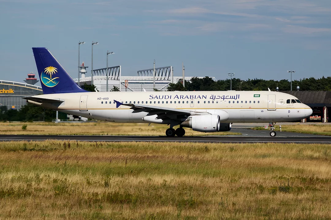 A SAUDIA SAUDI ARABIAN AIRLINES PASSENGER PLANE SITS ON AN AIRPORT RUNWAY.