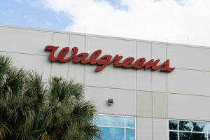 A WALGREENS SIGN CAN BE SEEN ON THE OUTSIDE OF THE STORE ABOVE A TREE AND BELOW A CLOUDY, BLUE SKY.