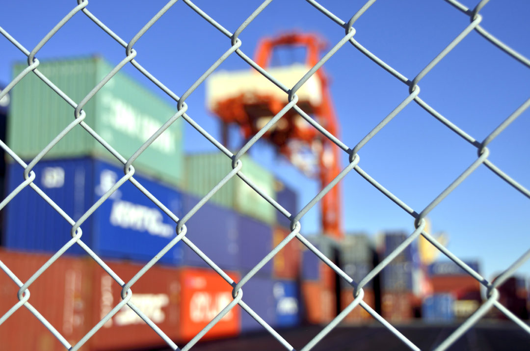 A METAL FENCE IN FRONT OF A CONTAINER YARD.