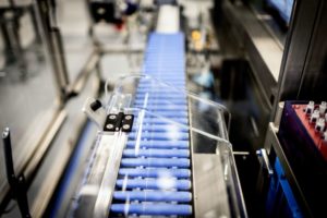 INJECTION PENS SIT ON A CONVEYOR BELT IN A FACTORY.