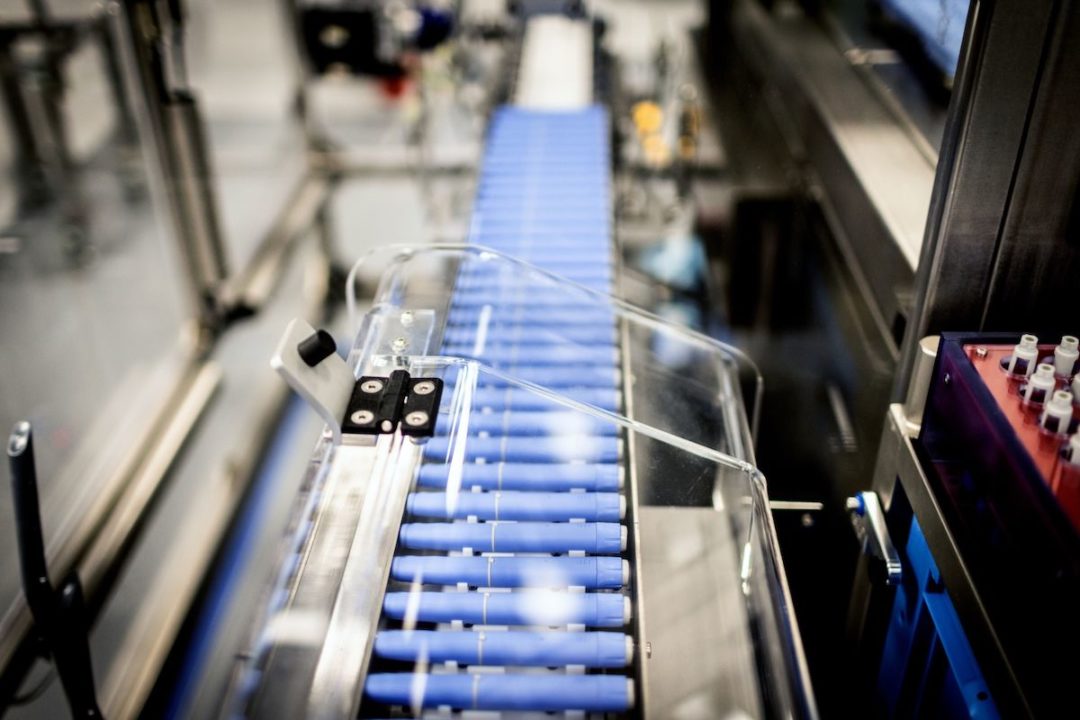 INJECTION PENS SIT ON A CONVEYOR BELT IN A FACTORY.