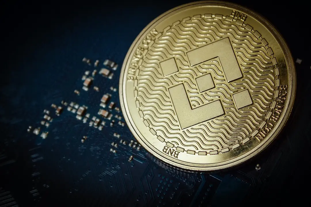 A GOLD BINANCE COIN SITS ON TOP OF A COMPUTER MOTHERBOARD.