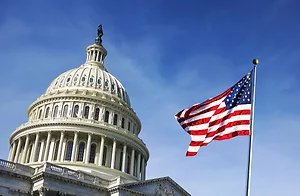 GROUND VIEW OF AN AMERICAN FLAG IN FRONT OF THE U.S. CAPITOL BUILDING UNDER A CLEAR, BLUE SKY.