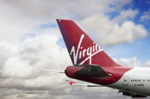 THE RUDDER OF A VIRGIN ATLANTIC LABELED PLANE SITS IN FRONT OF A CLOUDY SKY.