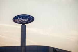 A FORD SIGN ABOVE A BUILDING CAN BE SEEN IN FRONT OF A YELLOW SKY.