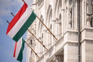 TWO RED, WHITE AND GREEN FLAGS OF HUNGARY HANG OUTSIDE A GRAND OLD BUILDING
