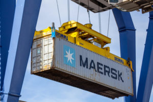 A MAERSK SHIPPING CONTAINER BEING HELD UP WITH A SHIPYARD CONTAINER CRANE.