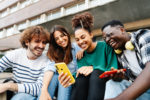 A GROUP OF YOUNG PEOPLE SMILING TOGETHER ARE LOOKING AT THEIR MOBILE PHONES.