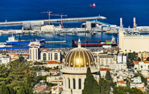 VIEW OF THE SHRINE OF BAB WITH THE HARNOR PORT OF HAIFA AND PORT CRANES IN THE BACKGROUND.