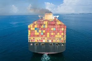 A CONTAINER SHIP AT SEA SPOUTS GREY SMOKE INTO THE SKY