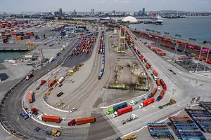 AN AERIAL SHOT OF A LONG, CURVING LINE OF TRUCKS BACKED UP AT A PORT