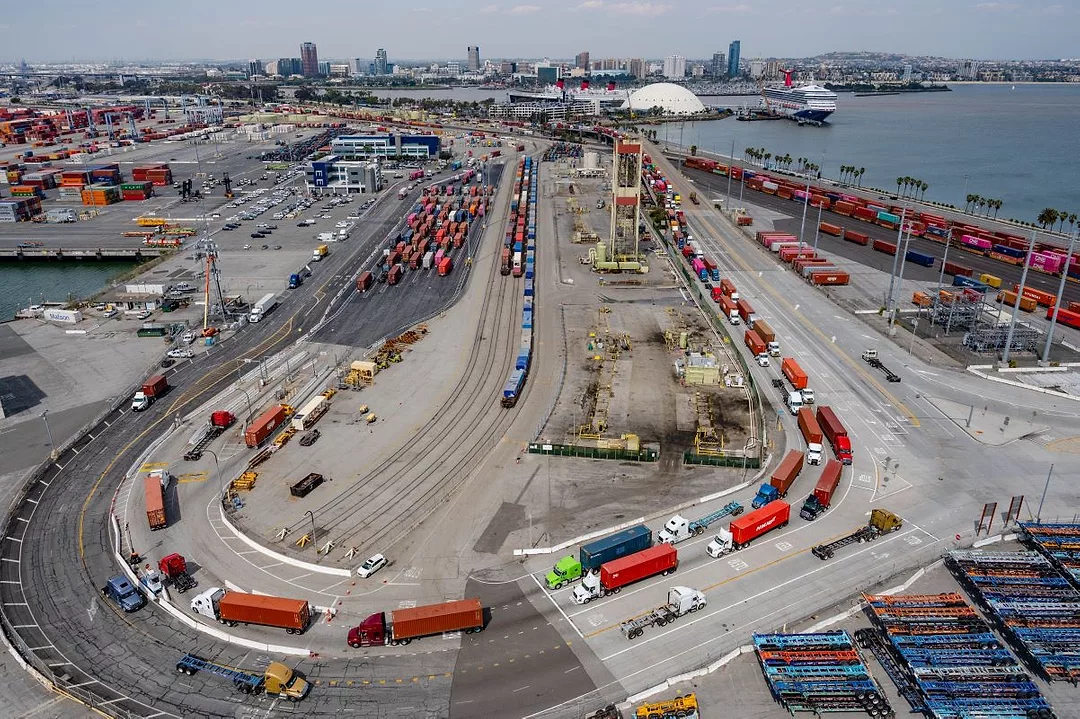 AN AERIAL SHOT OF A LONG, CURVING LINE OF TRUCKS BACKED UP AT A PORT