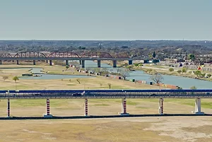 LONG RAIL AND ROAD BRIDGES CROSS A DRY, FLAT PLAIN CONTAINING A SNAKING RIVER