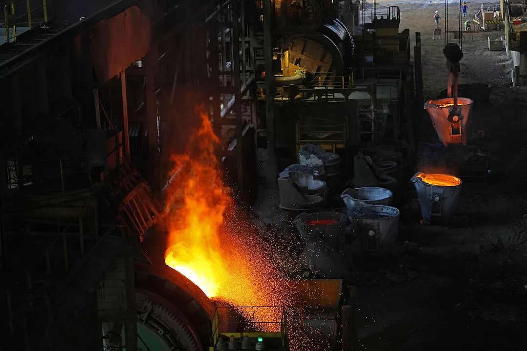 NICKEL ORE CONVERSION AT A PROCESSING PLANT. A LARGE FLAME BILLOWS FROM A FURNACE. 
