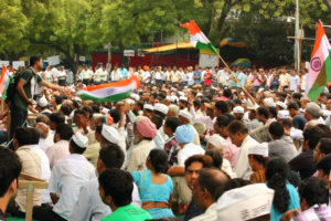 DOZENS OF PEOPLE TAKE PART IN A PUBLIC PROTEST. INDIAN FLAGS ARE BEING WAVED IN THE CROWD.