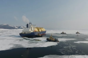 A LIQUIFIED NATRUAL GAS CARRIER TRAVELING ON AN ICY BODY OF WATER SURROUNDED BY THREE SMALLER BOATS.