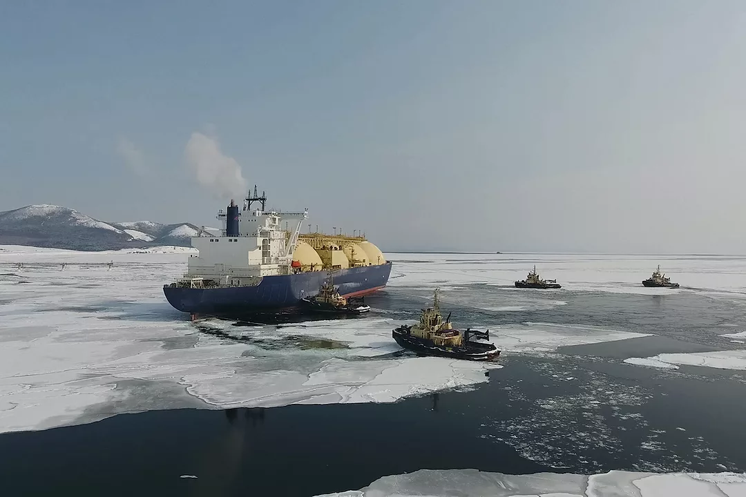 A LIQUIFIED NATRUAL GAS CARRIER TRAVELING ON AN ICY BODY OF WATER SURROUNDED BY THREE SMALLER BOATS.