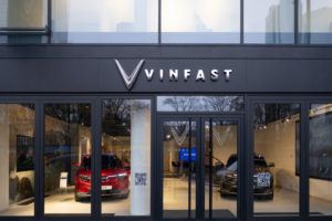 EXTERIOR OF A VINFAST DEALERSHIP. THE DEALERSHIP'S LARGE WINDOWS SHOW EVS AND CUSTOMERS INSIDE.