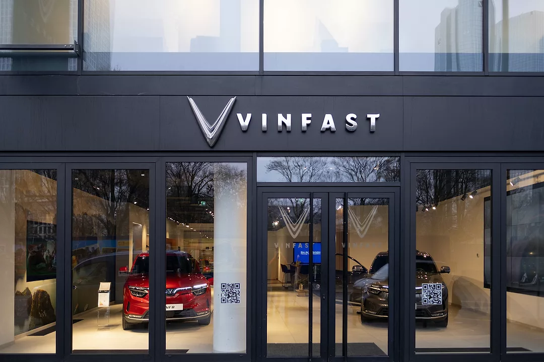 EXTERIOR OF A VINFAST DEALERSHIP. THE DEALERSHIP'S LARGE WINDOWS SHOW EVS AND CUSTOMERS INSIDE.