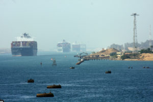 THREE LARGE CONTAINER SHIPS CAN BE SEEN TRAVELING ON A BODY OF WATER NEAR A SMALL HARBOR.