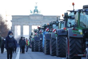 A ROW OF TRACTORS LINES UP IN FRONT OF THE BRANDENBERG GATE.