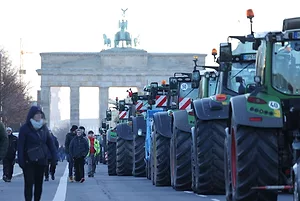 A ROW OF TRACTORS LINES UP IN FRONT OF THE BRANDENBERG GATE.
