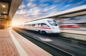 HIGH-SPEED TRAIN IN MOTION PASSING A RAILWAY STATION AS THE SUN SETS.