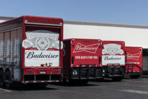 FOUR RED BUDWEISER-BRANDED DELIVERY TRUCKS ARE PARKED IN A LOADING DOCK.